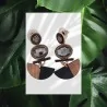 Boucles d'oreilles artisanales en bois, pierre et métal doré sur fond de feuilles vertes